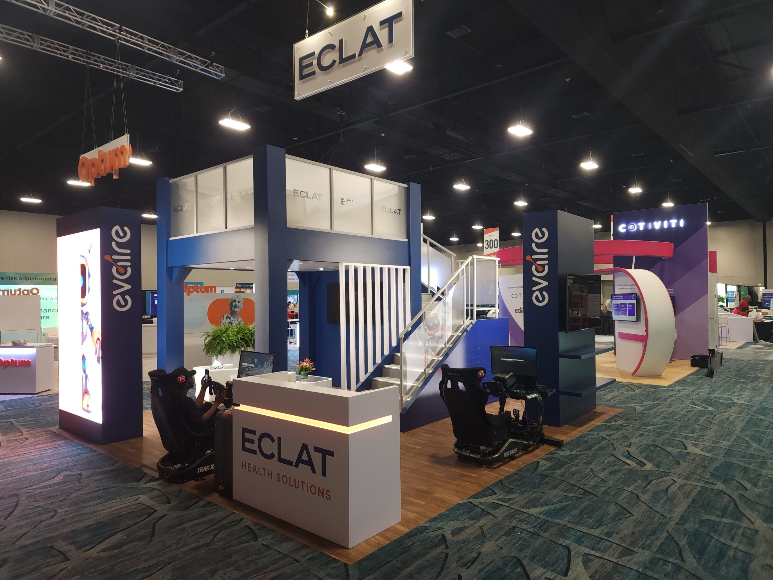 Custom 20x20 double-deck trade show exhibit rental by FX Design Group for ECLAT Health Solutions at RISE National 2026 Conference with reception counter, staircase, and interactive demo stations.